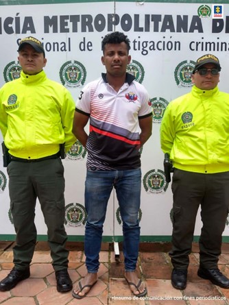En la fotografía aparece un hombre capturado junto a dos uniformados de la Policía Nacional. En la parte posterior se ve un banner de la Policía Nacional.