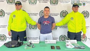 El imputado se encuentra en custodia por un uniformado de la Policía Nacional. Detrás hay un backing de la Policía y los elementos incautados.