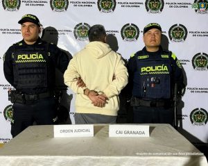 En la fotografía se aprecia de pie, con los brazos atrás y de espaldas a la cámara Javier Antonio Aricapa Parra. Viste con buso de color amarillo crema y pantalón de color gris. A los extremos hay uniformados de la Policía Nacional. Delante de ellos hay una superficie y sobre ella se aprecian dos letreros que dicen: ‘Orden Judicial’ y ‘CAI Granada’. En la parte posterior hay un pendón institucional de la Policía.