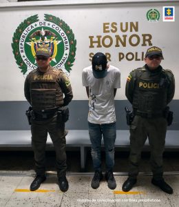 En la fotografía aparece un hombre capturado, junto a dos agentes de la Policía Nacional. En la parte posterior de la imagen se ve un banner de la Policía.