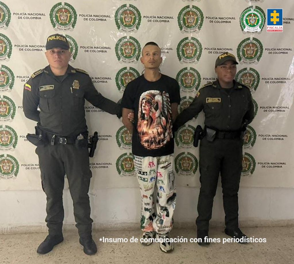 En la fotografía se aprecia de pie y con los brazos atrás a Jeferson Sánchez Maya. Viste camiseta de color negro con estampado de un indígena en la parte frontal; pantalón de color blanco con estampados de color negro y rojo, así como zapatillas blanca con negro. A sus extremos hay uniformados de la Policía Nacional. Detrás de ellos hay un pendón institucional de la Policía.