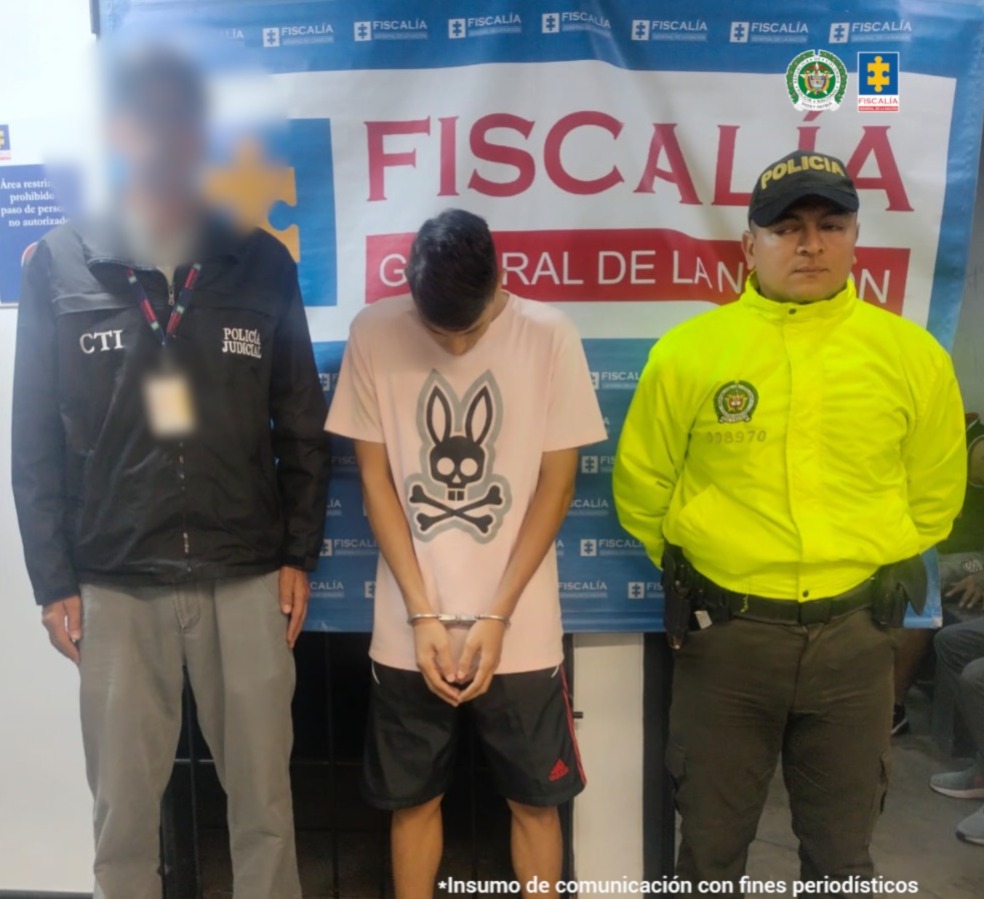 Se visualiza al capturado junto a un investigador del CTI y un uniformado de la Policía Nacional. En la parte posterior se ubica el banner que identifica a la Fiscalía General de la Nación.