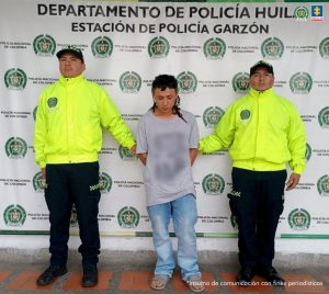 El imputado se encuentra en custodia por dos uniformados de la Policía Nacional. Detrás se observa un backing de la Policía.