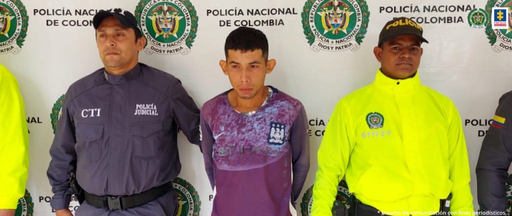 En la fotografía aparece un capturado, junto a personal de Policía Nacional. En la parte posterior de la imagen se ven banners de Policía Nacional y la Fiscalía General de la Nación.