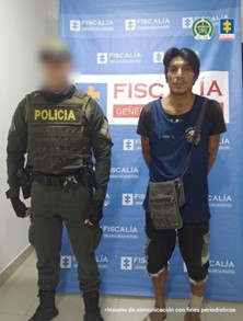 Se visualiza al capturado junto a un uniformado de la Policía Nacional. Detrás el banner que identifica a la Fiscalía General de la Nación