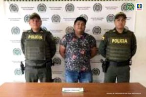 En la fotografía aparece un hombre capturado, acompañado de dos uniformados de la Policía. En la parte posterior un banner con logos de la entidad.