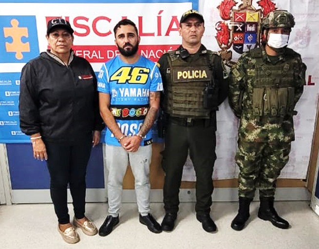 en la imagen se ve una persona detenida bajo custodia de investigadores del CTI, Policía y Ejército. Detrás suyo un backing de la Fiscalía.  