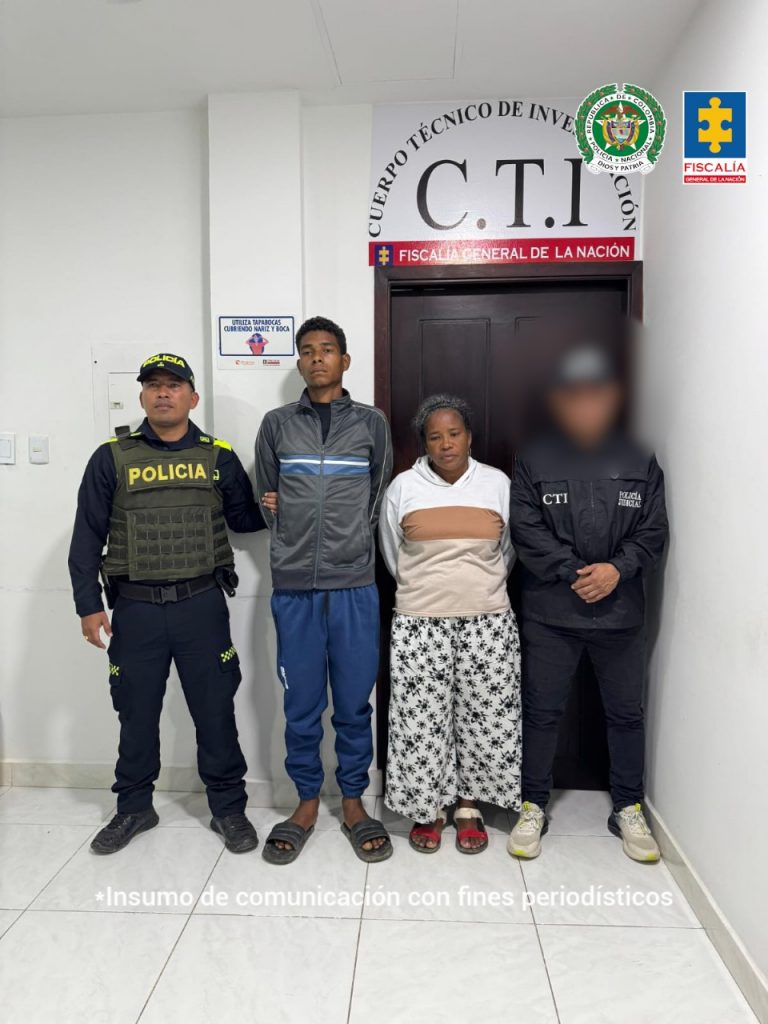 En la imagen aparece un muchacho de saco gris y sudadera azul, junto a una señora quien tiene un buso blanco con café, entre dos uniformados del CTI y la Policía Nacional.