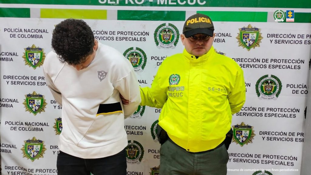 Se visualiza al capturado junto a un uniformado de la Policía Nacional. Detrás de ellos el banner que identifica a la Policía Nacional