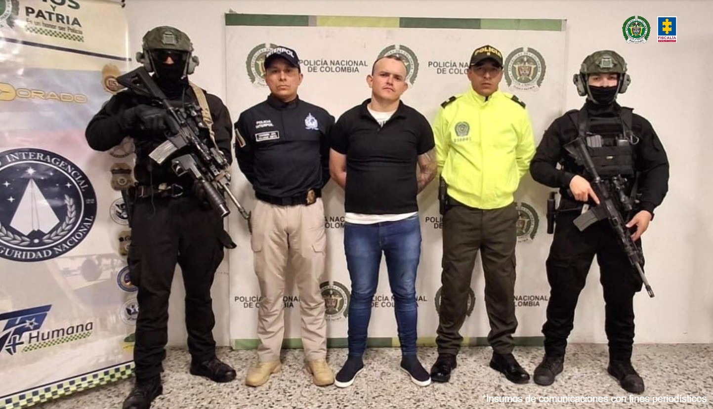 El capturado aparece en el centro de la imagen, de mie, con las manos esposadas atrás. Está rodeado de miembros de la Policía e Interpol.