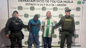 En la fotografía aparecen dos capturados junto a personal de Policía Nacional y Fiscalía General de la Nación. En la parte posterior de la imagen se ven banners de Policía Nacional y la Fiscalía General de la Nación.