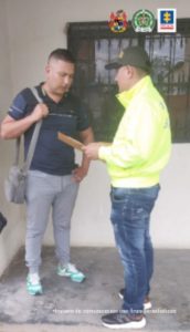 En la fotografía aparece un capturado junto a personal de Policía Nacional. En la parte posterior de la imagen se ven banners de Ejército Nacional, Policía Nacional y la Fiscalía General de la Nación.