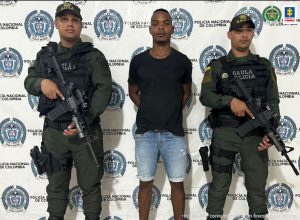 En la fotografía aparece un hombre capturado, acompañado de dos uniformados de La Policía. En la parte posterior un banner con logos de la entidad.