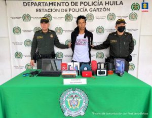 El procesado se encuentra esposado y en custodia por uniformados de la Policía Nacional. Detrás suyo un backing de la Policía y se observan los elementos incautados.