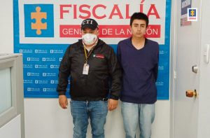 capturado de frente manos atrás custodiado por Investigador del CTI de la Fiscalía. Detrás Banner de Fiscalía.