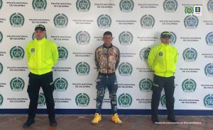 Se observa el capturado de frente y a cada costado un uniformado de Policía Nacional. Atrás un pendón de Policía Nacional