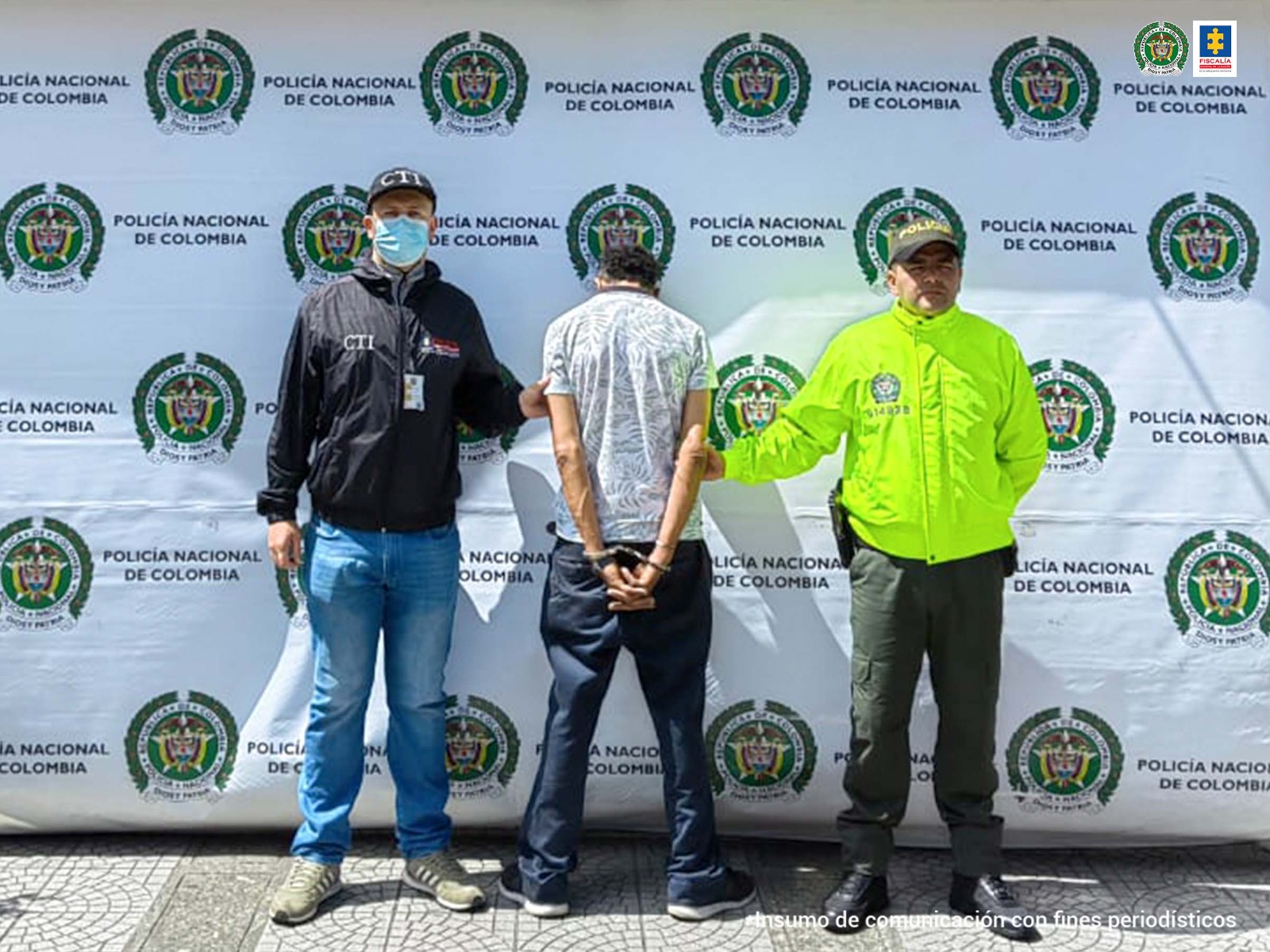 En la foto aparece Jhovanny Antonio Hernández Betancur acompañado a cada lado de un funcionario de CTI y de la Policía. Al fondo el backing con logos de la Policía.