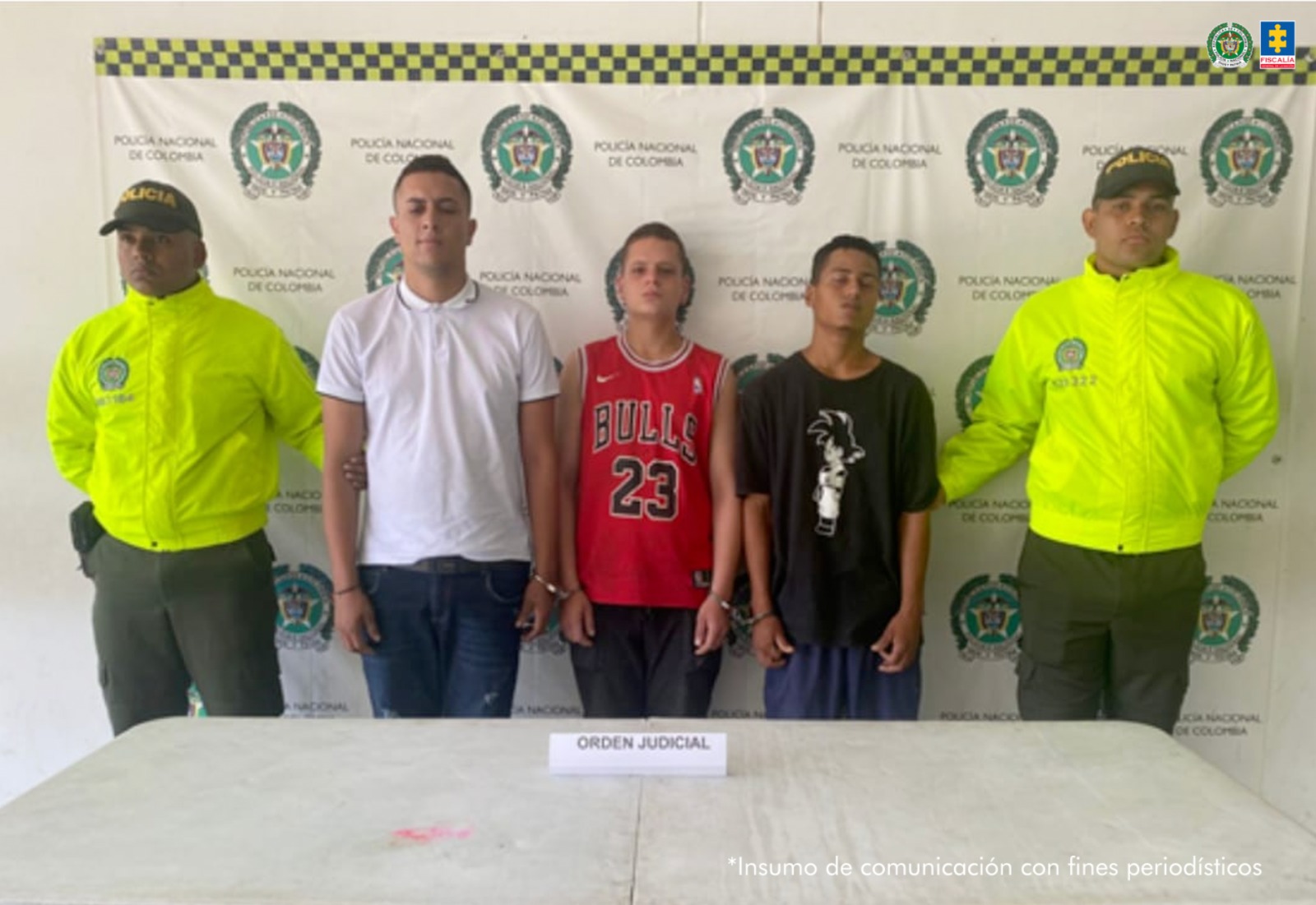 En la fotografía se aprecian de pie y esposados entre sí a Jimmy Alexander González Ariza, alias El Yimmi; Johan Alejandro Plaza González, alias Chicho; y Alexánder Tenorio Rivera, alias Cabezón. Uno viste camiseta de manga corta y cuello de color blanco y jean azul oscuro. Otro viste camiseta deportiva sin mangas, de color rojocon ribetes negros y blancos, así como impreso la palabra ‘Bulls’ y el número ‘23’, pantalón negro. Un tercero usa camiseta de manga corta de color negro con estampado y pantalón azul. A los extremos de ellos hay uniformados de la Policía Nacional. Delante de ellos hay una superficie blanca y sobre ella un letrero que dice: ‘Orden judicial’. Detrás de ellos hay un pendón institucional de la Policía.
