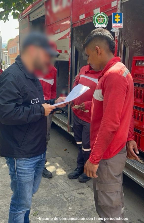 En la fotografía, tomada en exteriores, se aprecia de perfil a Johan Andrés Buitrago Castrillón. Viste camibuso de color rojo con pantalón gris. Frente a él hay un servidor del CTI de la Fiscalía quien lee un documento que tiene en sus manos.
