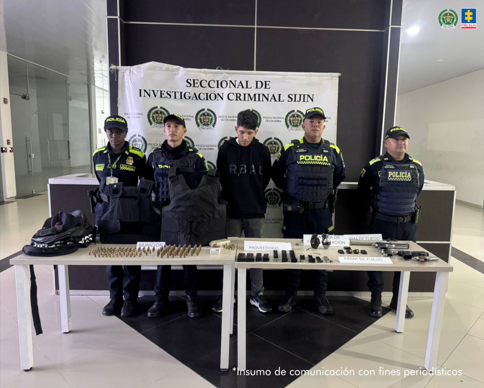 Se visualiza al capturado junto a uniformados de la Policía Nacional. Frente a ellos una mesa con los elementos incautados. Detrás de ellos el banner que identifica a la Policía Nacional.