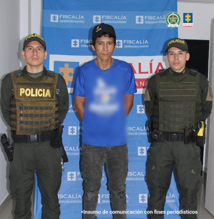 Se visualiza al capturado junto a dos uniformados de la Policía Nacional.Detrás de ellos el banner que identifica a la Fiscalía General de la Nación. Policía Nacional.
