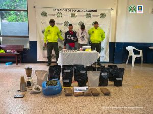 En la fotografía se aprecia de pie a Johann David Caballos Barón y Oscar Eduardo Franco Mezú. Uno de ellos viste buso negro con estampado blanco y camisa roja debajo de éste; así como jean azul. El otro viste buso blanco con estampado negro de Tío Rico y pantalón verde. Al lado y lado de ellos hay uniformados de la Policía Nacional. Delante de ellos hay una mesa y sobre ella hay varias bolsas plásticas pequeñas; varias bolsas plásticas de color rosadom amarillo y negro; así como un letrero que dice ’Base de coca’. En el piso se aprecia una licuadora y varios paquetes de bolsas negras, transparentes y azul; igualmente, un letrero que dice: ‘Marihuana’. En la parte de atrás de ellos hay un pendón institucional de la Policía Nacional.