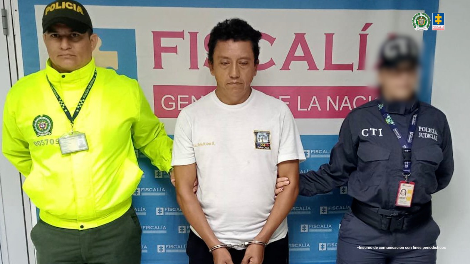 capturado de frente custodiado por investigador del CTI de la Fiscalía y un policía. Detrás banner de la Fiscalía.