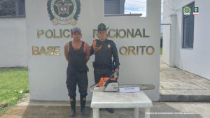 En la imagen se ve al capturado en custodia por un uniformado de la Policía Nacional. Se observa una mesa con la guadaña incautada y detrás hay un letrero de la Policía Nacional.