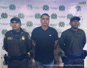 En la fotografía aparece de pie y con los brazos atrás John Jairo Soto Raigosa. Viste con camisa de cuello y mangas cortas, de color verde oscuro; con ribetes blancos en mangas y cuello; jean azul. En sus extremos hay uniformados de la Policía Nacional. Detrás de ellos hay un pendón institucional de la Policía.