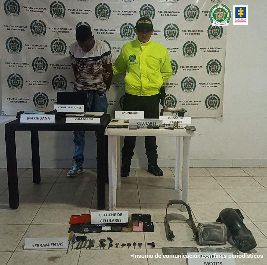 En la fotografía aparece un capturado junto a personal de Policía Nacional. En la parte posterior de la imagen se ven banners de Policía Nacional y la Fiscalía General de la Nación.