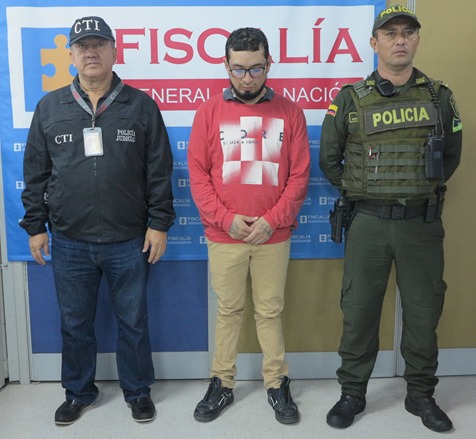 en la imagen se ve una persona detenida bajo custodia de la Policía y el CTI. Detrás suyo un backing de la Fiscalía.  