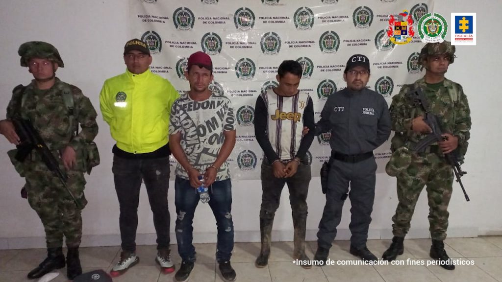 En la fotografía aparecen dos capturados, junto a personal de Fiscalía General de la Nación, Ejercito Nacional y Policía Nacional. En la parte posterior de la imagen se ven banners de Ejército Nacional, Policía Nacional y la Fiscalía General de la Nación.