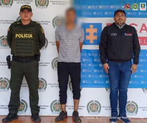 En la imagen se ve una persona detenida bajo custodia de dos uniformados del Ejército y un investigador del CTI. Detrás suyo backings institucionales.