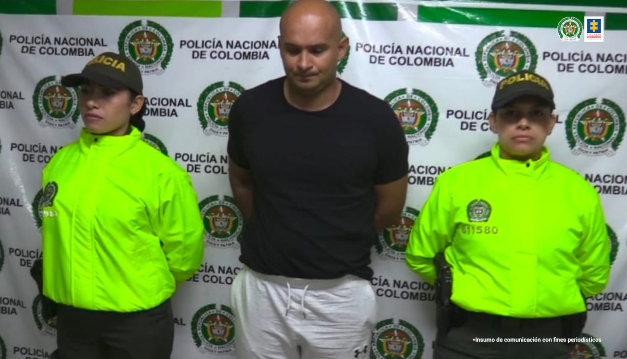 En la fotografía aparece un hombre capturado junto a dos agentes de la Policía Nacional. En la parte posterior se ve un banner de la Policía Metropolitana Cali