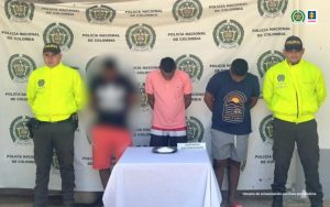 En la fotografía aparecen dos hombres capturados, acompañados de dos uniformados de La Policía. En la parte posterior un banner con logos de la entidad.