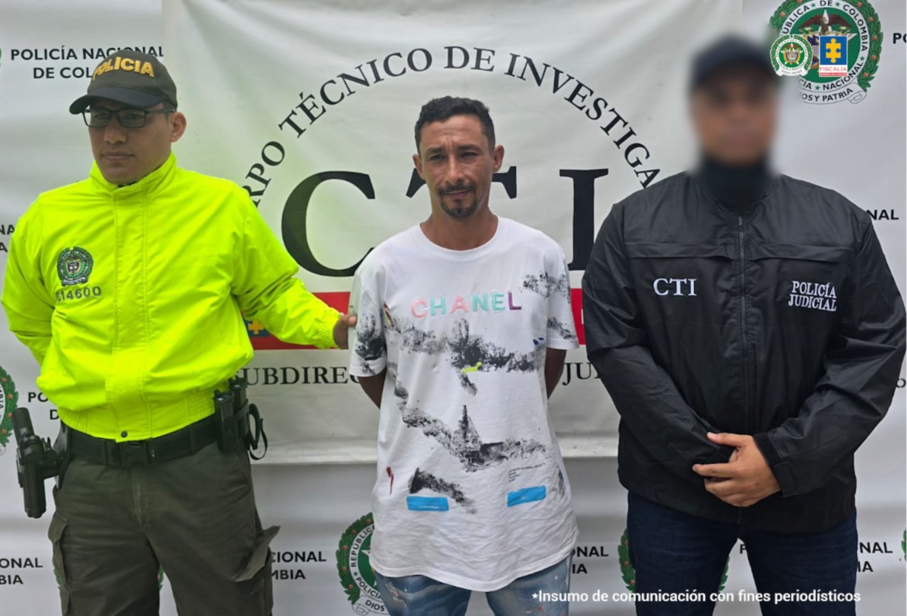 En la imagen está el capturado con un servidor del CTI y otro de la Policía Nacional a los lados y un pendón del CTI al fondo
