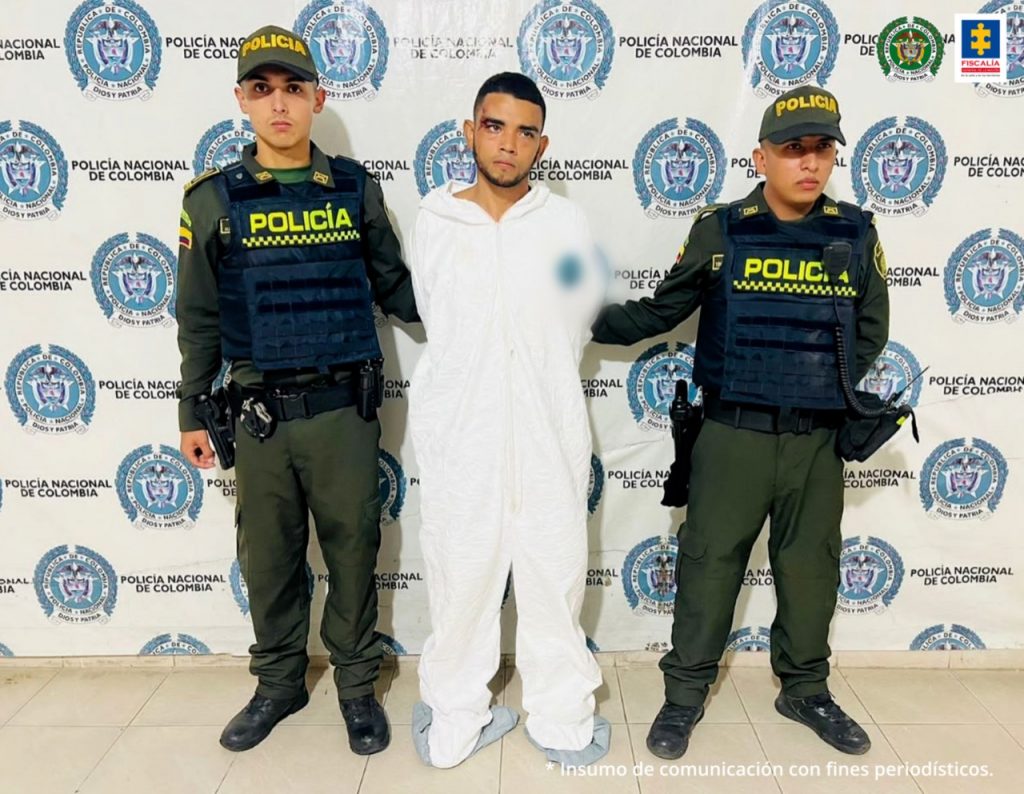 En la fotografía un hombre capturado, junto a dos uniformados de la Policía Nacional. En la parte posterior de la imagen se ve un banner de la entidad.