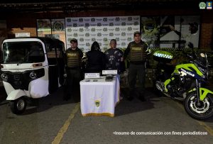 La fotografía fue tomada en horas de la noche. En ella aparecen de pie y de espaldas a la cámara Jorge Enrique  Albán Cruz y a María del Carmen David Chávez. La mujer viste con buso negro y capucha. El viste con camiseta negra, manga corta y con estampados de palmeras grises. A sus extremos hay uniformados de la Policía Nacional. Delante hay una mesa con mantel blanco, ribetes dorados y el escudo de la Policía; sobre ella hay dos celulares  y paquetes de color negro. Asimismo, hay dos letreros que dicen: ’Clorhidrato de cocaína’ y ‘Celulares incautados’. Al extremo izquierdo de la fotografía hay un motocarro de color blanco. En la parte posterior hay un pendón institucional de la Policía.