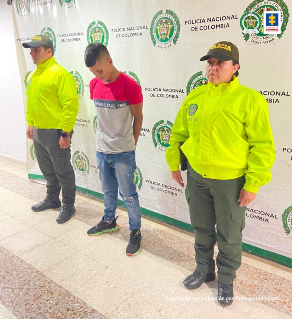 En la fotografía aparece un capturado, junto a personal de Policía Nacional. En la parte posterior de la imagen se ven banners de Policía Nacional y la Fiscalía General de la Nación.