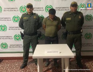En la fotografía aparece de pie, la cabeza agachada y con los brazos atrás, Jorge Evelio Quitián Salazar. Viste con camiseta verde de manga corta. A lado y lado de él hay uniformados de la Policía Nacional. Delante de ellos hay una mesa cuadrada y sobre ella hay un letrero que dice: ‘Orden judicial. Detrás de ellos hay un pendón institucional de la Policía.