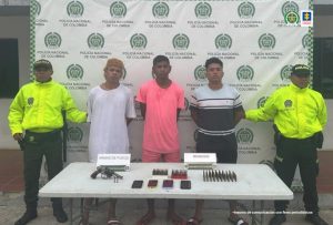 En la fotografía aparecen tres hombres capturados, acompañados de dos uniformados de la Policía Nacional. En la parte posterior un banner con logos de la entidad.