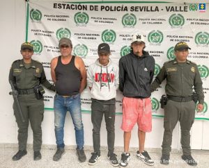 En la fotografía aparecen de pie y con los brazos atrás de los cuatro hombres con corras. Dos de ellos visten con busos de color blanco y negro, pantaloneta rosada y pantalón negro largo. El otro viste camisa esqueleto de color negro y jean azul desgastado. En los extremos de ellos hay uniformados de la Policía Nacional. Detrás de ellos hay un pendón institucional de la Policía.