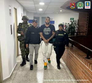 Fiscal Martha Mancera, Martha Mancera, Fiscal Mancera La fotografía se aprecia en acción de caminata, en un pasillo, a José Alberto Posada Caicedo, alias Político o Mateo. Viste camiseta de manga corta negra, con estampado circular a la altura del pecho de colores blanco, verde y negro; pantalón de sudadera gris y zapatillas de color verde con naranja. Al lado derecho de él hay un servidor del CTI de la Fiscalía y un uniformado del Ejército Nacional. Al lado izquierdo hay una uniformada de la Policía Nacional.