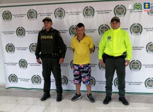 El procesado se encuentra esposado y en custodia por uniformados de la Policía. Detrás suyo hay un backing de la Policía.