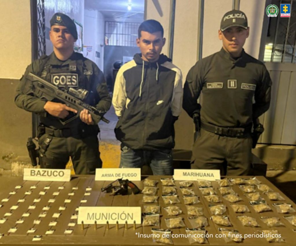 En la fotografía se aprecia de pie y con los brazos atrás a José Andrés García Giraldo. Viste buzo de manga larga de color marrón con mangas beage y jean azul. A los extremos hay uniformados de la Policía Nacional. Delante de ellos hay una superficie y sobre ella hay un arma de fuego, munición y bolsas plásticas pequeñas.