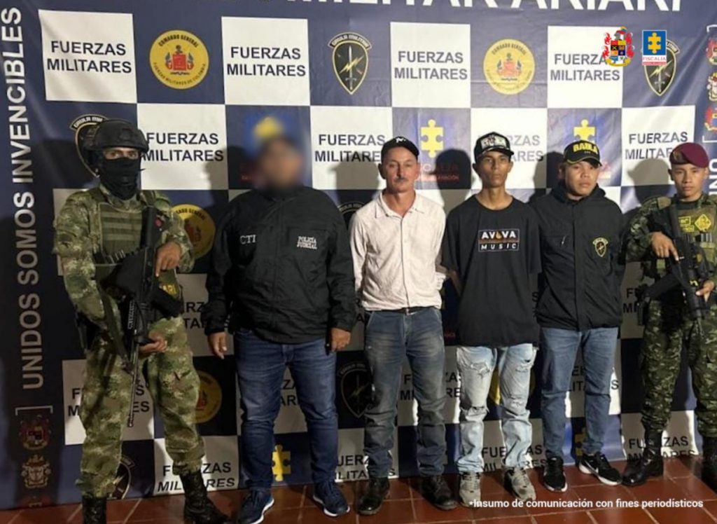 capturados de frente custodiados por investigadores del CTI de la Fiscalía y soldados. Detrás banner del grupo Gaula.