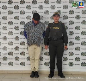  El procesado se encuentran esposado y en custodia por un uniformado de la Policía Nacional. Detrás suyo un backing de la Policía.