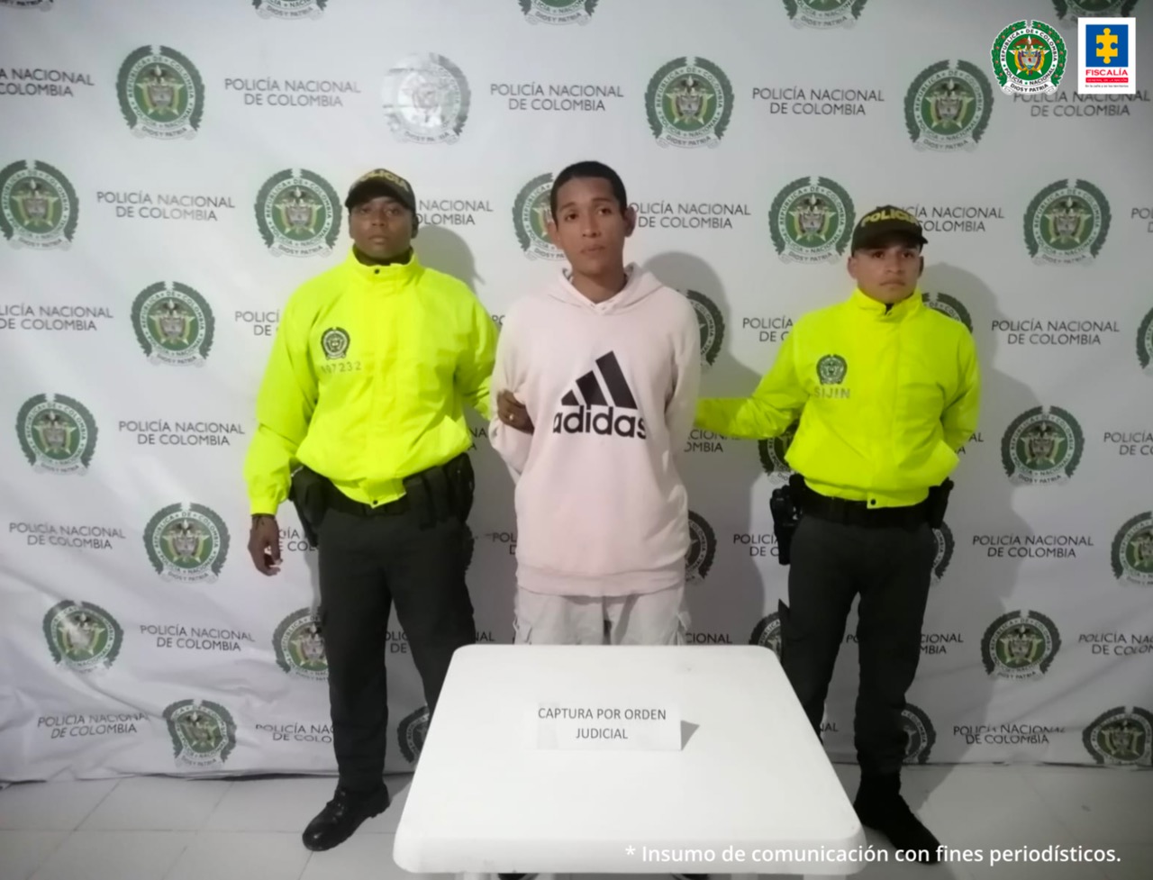 En la imagen aparece el capturado con 2 miembros de la policía Nacional, uno a cada lado, y una mesa en el centro con un letrero en donde se aclara que la captura fue por orden judicial.