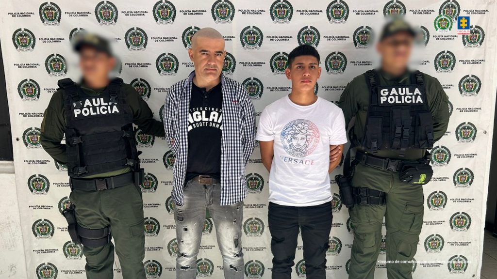 Los capturados se encuentran de frente y custodiados por dos uniformados del Gaula de la Policía Nacional. Detrás se observa un backing de la Policía Nacional.