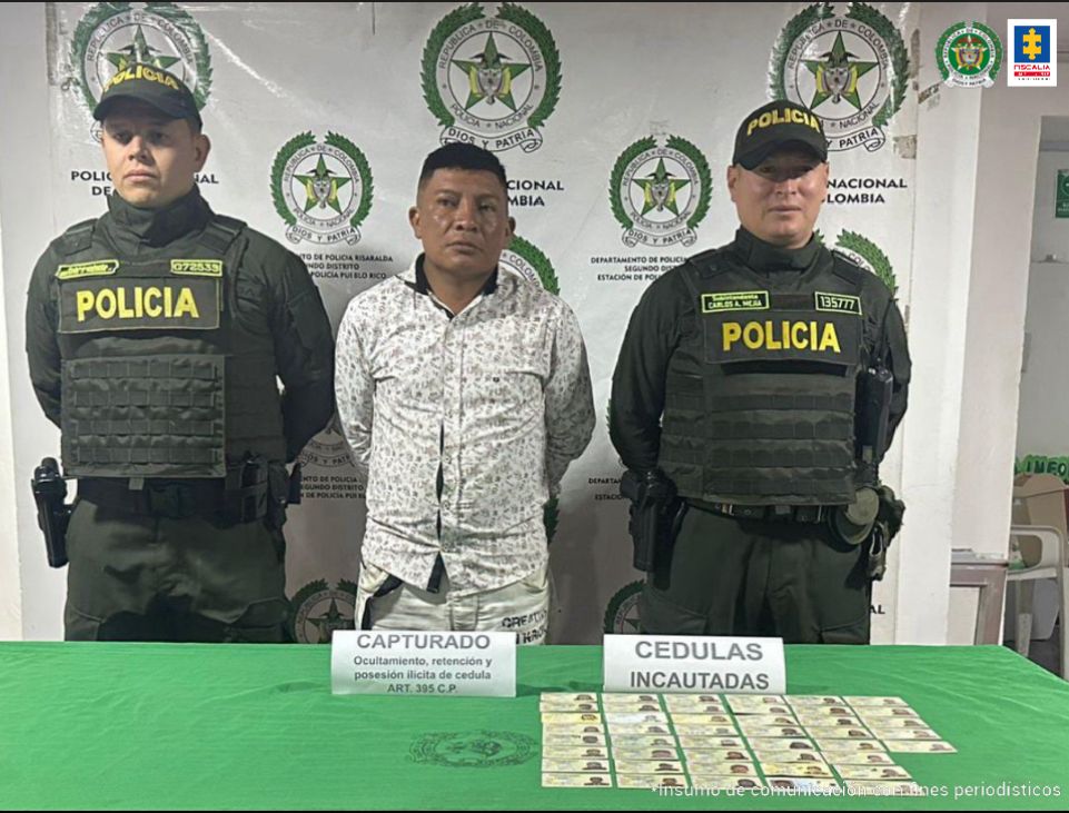 En el centro se observa al capturado y a cada costado un funcionario de Policía Nacional. Al frente una mesa con el material incautado